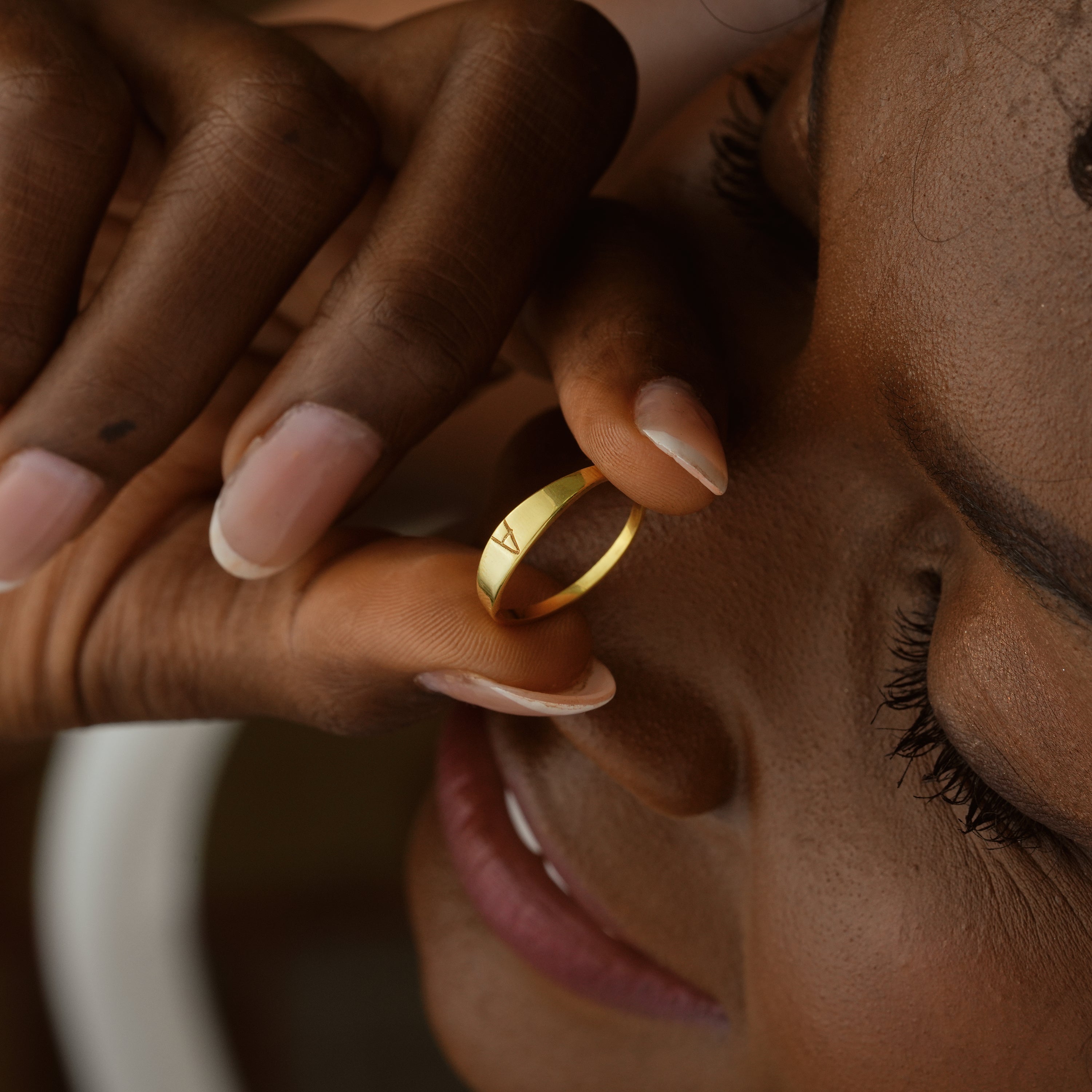 Close-up of a woman holding a gold Personalized Name Ring against her face, showcasing its elegant design.