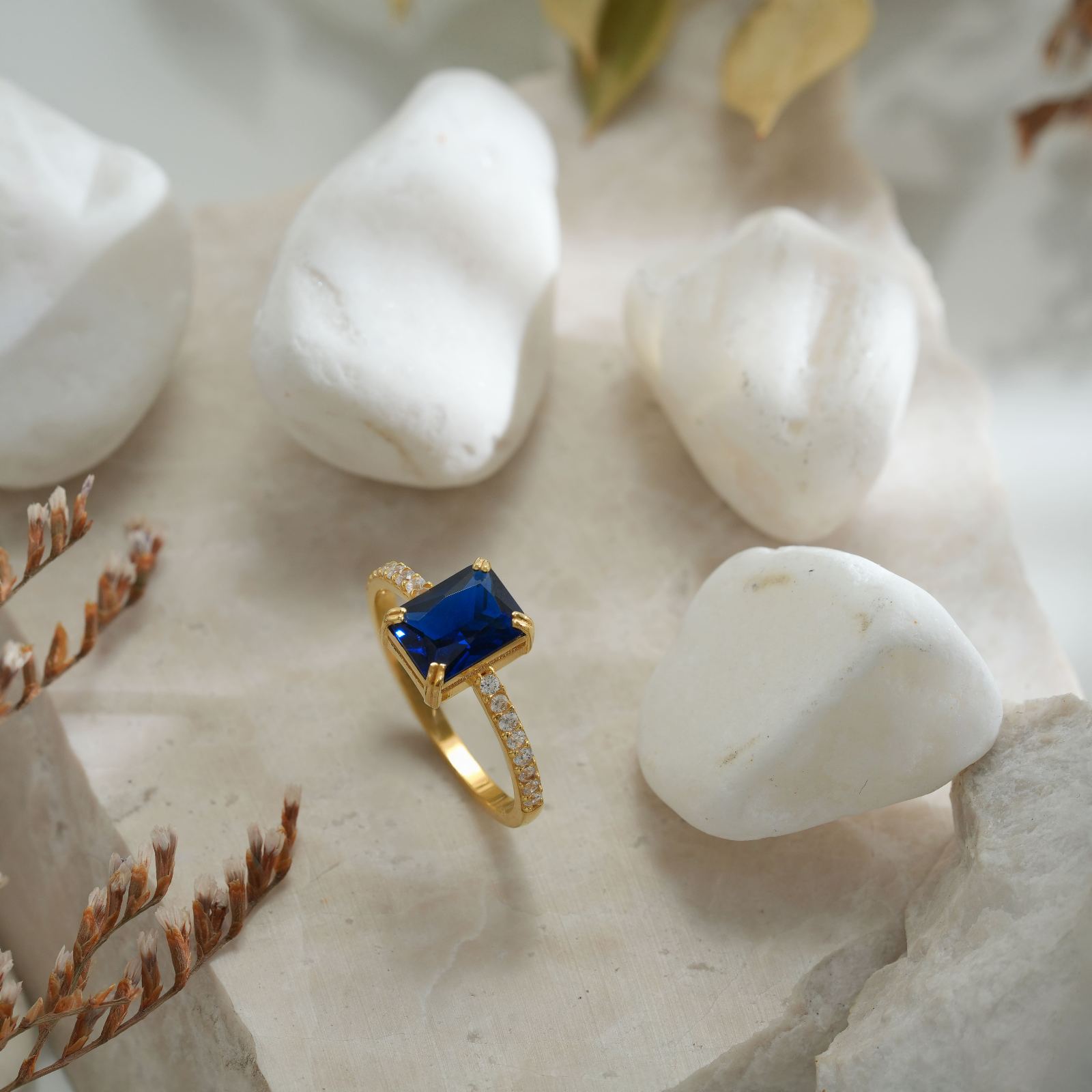 Rectangle Statement Birthstone Ring featuring a blue stone set in gold with sparkling accents on a stone background.