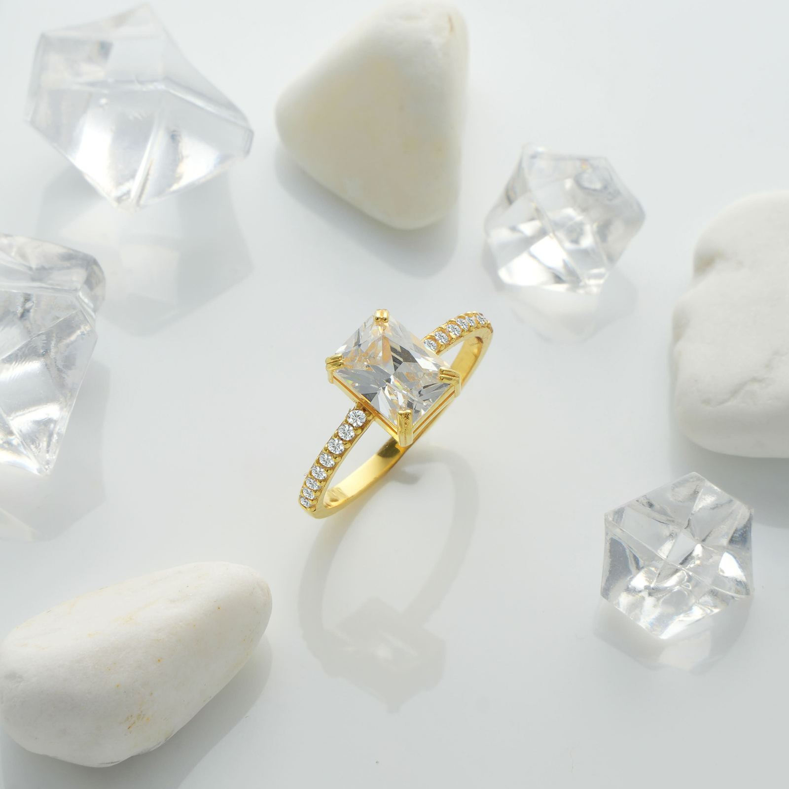 Rectangle Statement Birthstone Ring set on white stones with clear crystals around, featuring a gold band and a sparkling center stone.