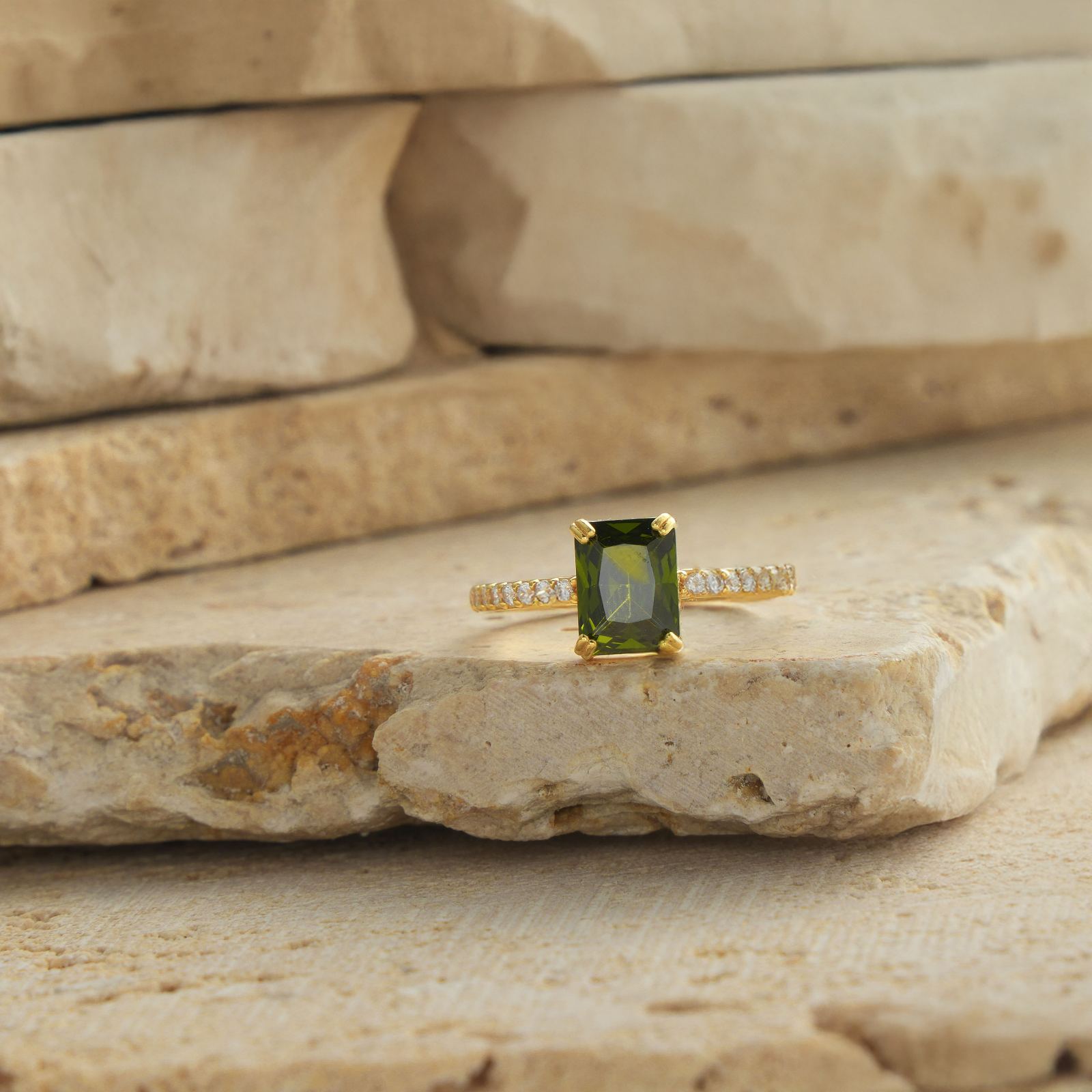 Rectangle Statement Birthstone Ring with a green gemstone set on a textured stone background.