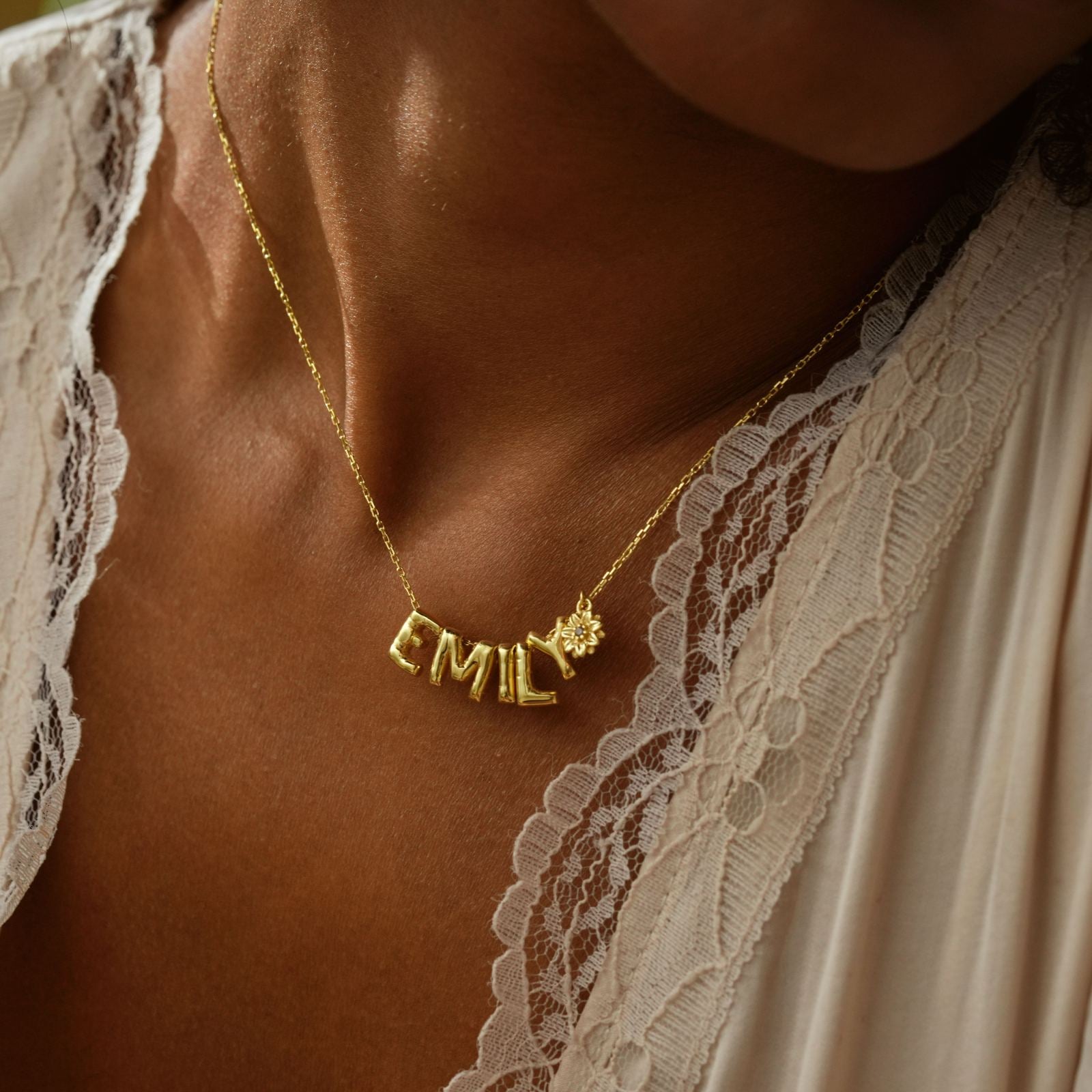 3D Bubble Letter Necklace with gold letters spelling EMIL and a birth flower design, worn on a lace top.