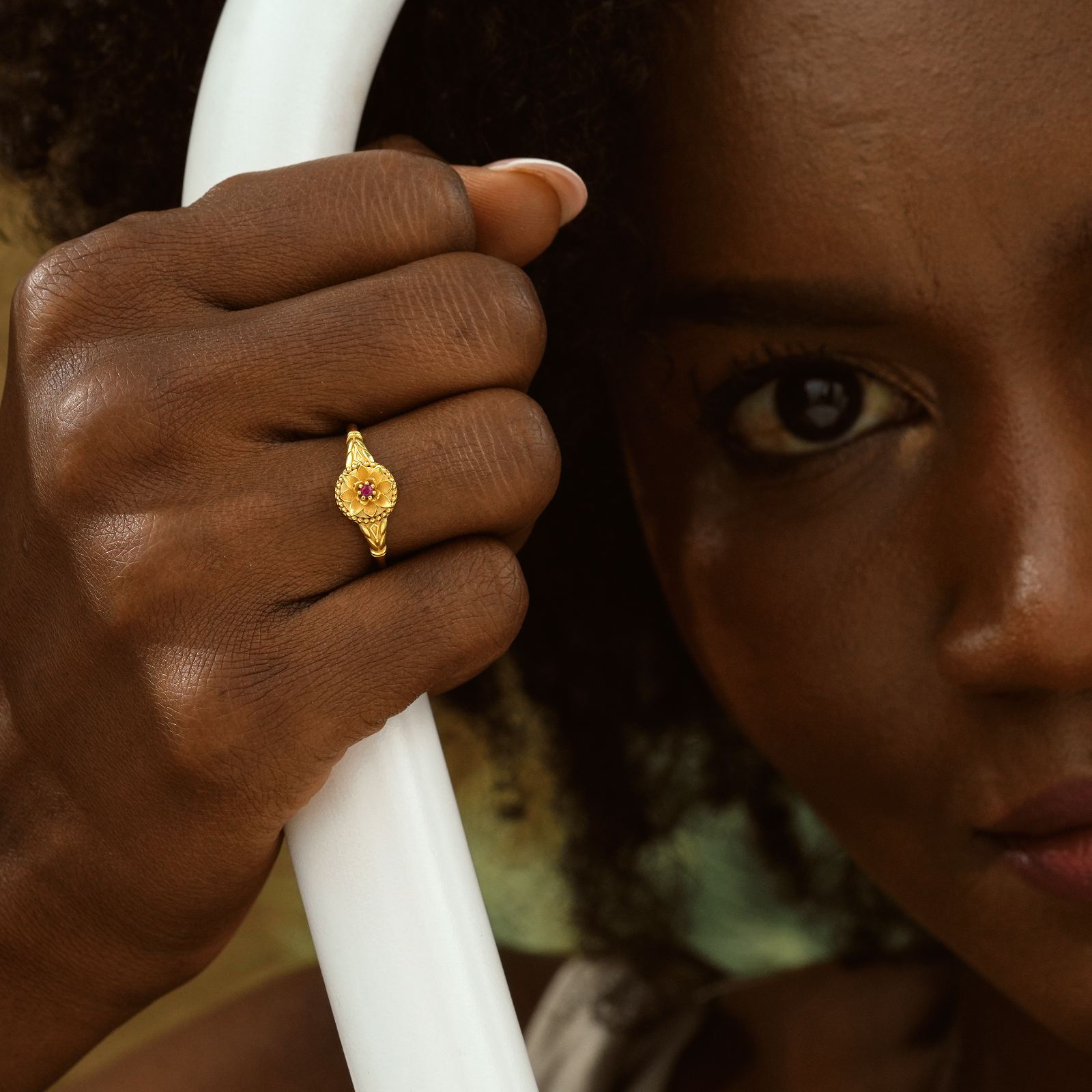 Close-up of a hand holding a white hoop, wearing a Custom Birth Flower Ring in gold vermeil with a gemstone.