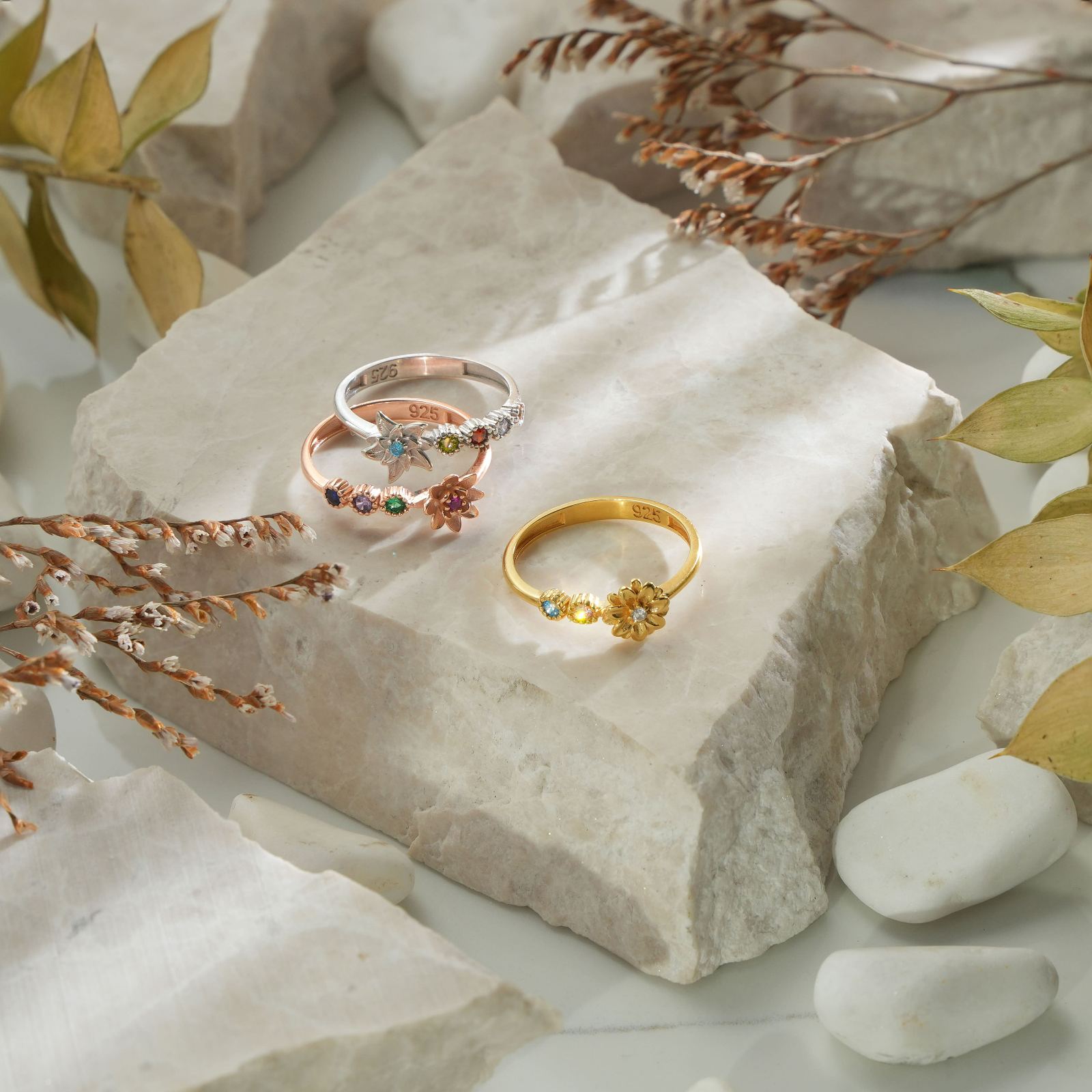 Custom Birth Flower Ring with Birthstone displayed on a stone surface among leaves and pebbles.