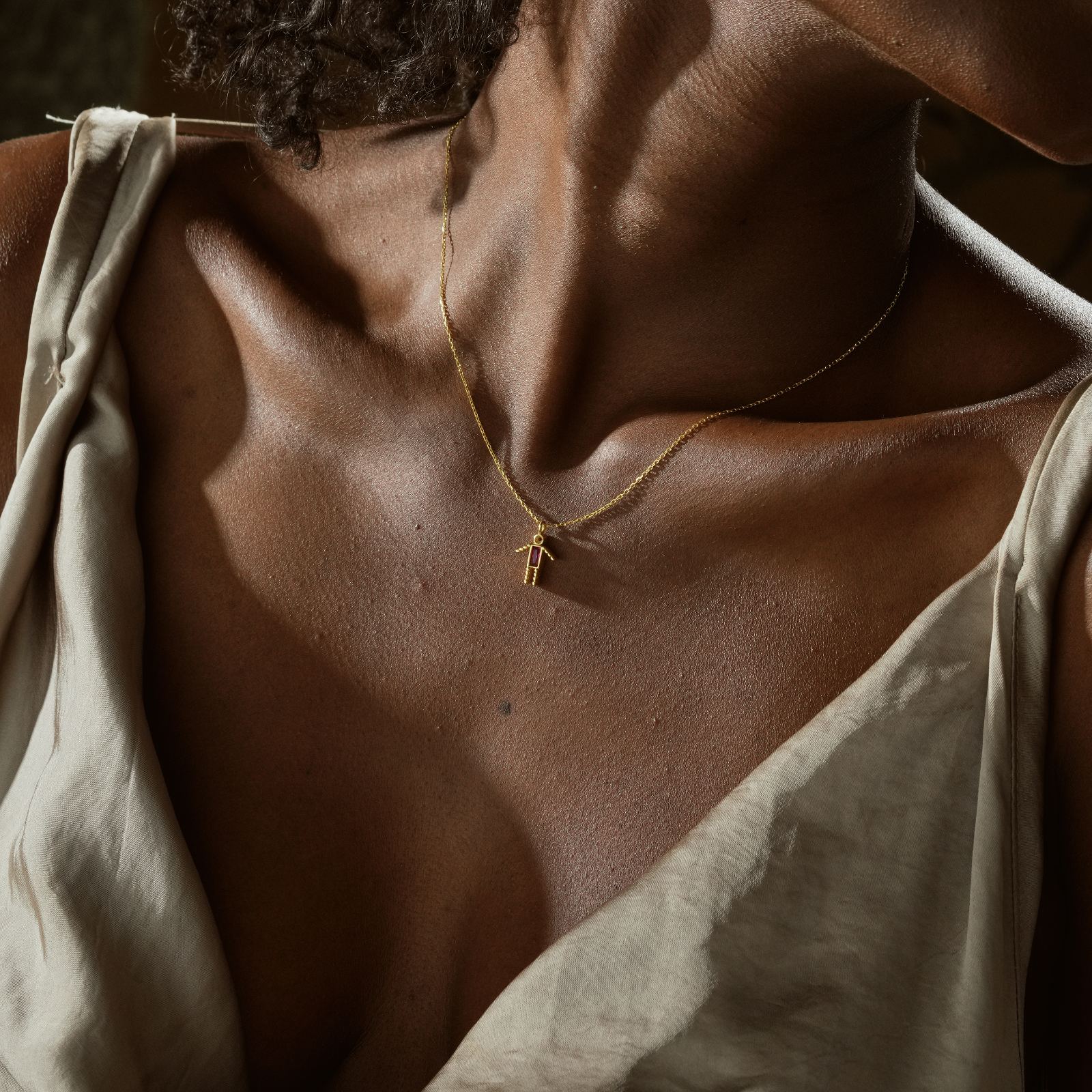 Close-up of a person wearing a Dainty Boy Birthstone Charm Necklace in gold, showcasing an elegant design on bare skin.