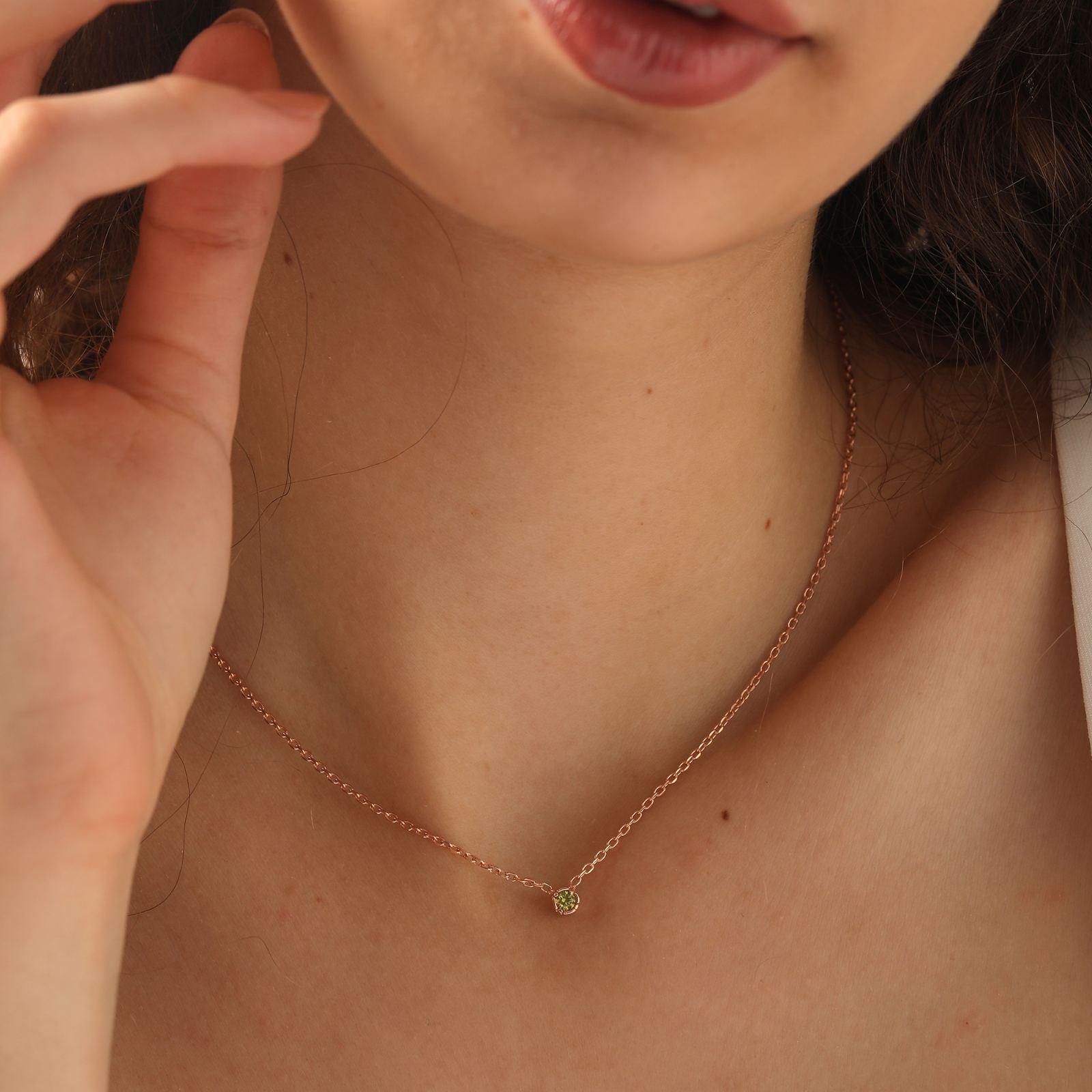 Close-up of a woman wearing a Personalized Birthstone Necklace with a green birthstone on a rose gold chain.