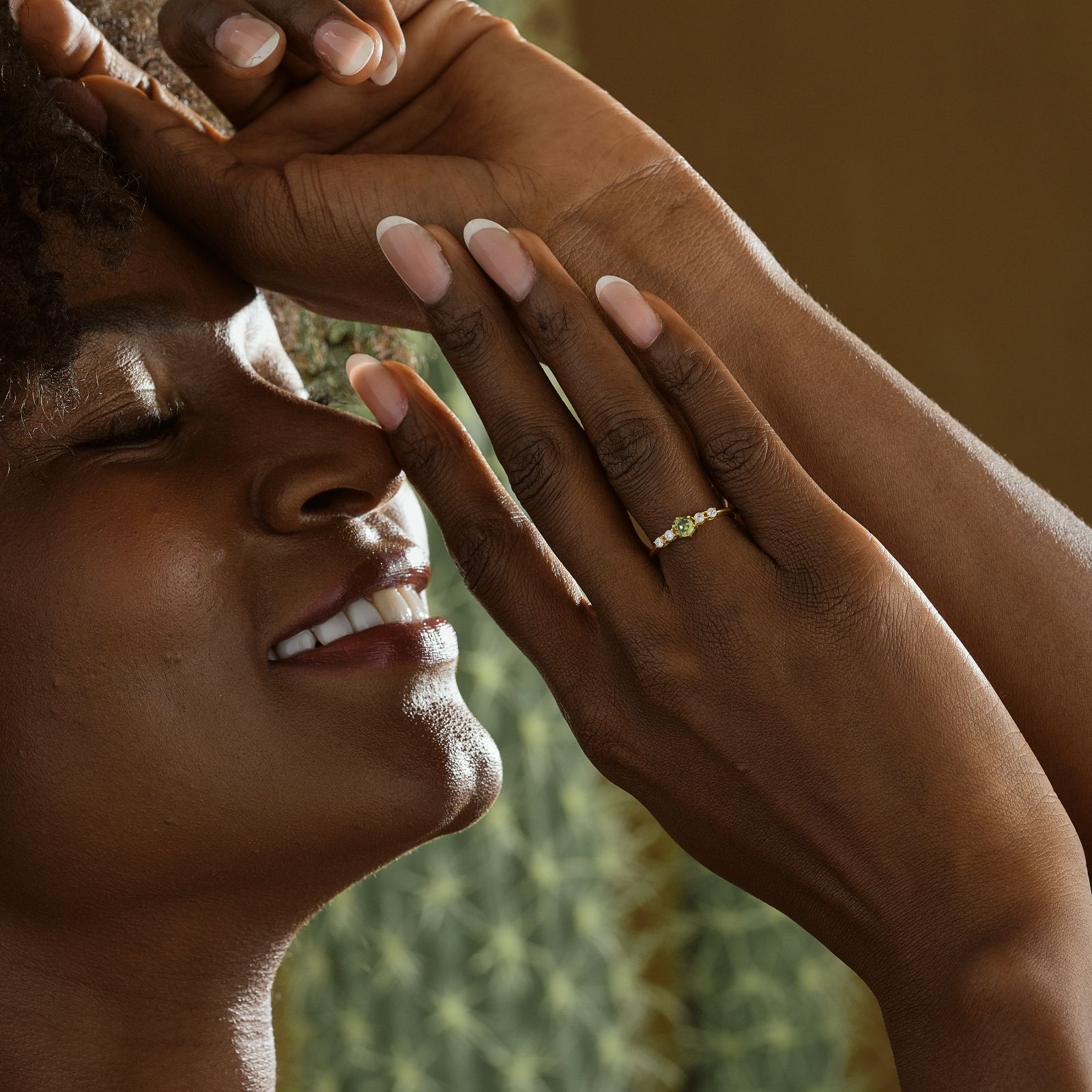 Woman showcasing a Round Cut Birthstone Ring with gold finish and gemstones, smiling gently in soft lighting.