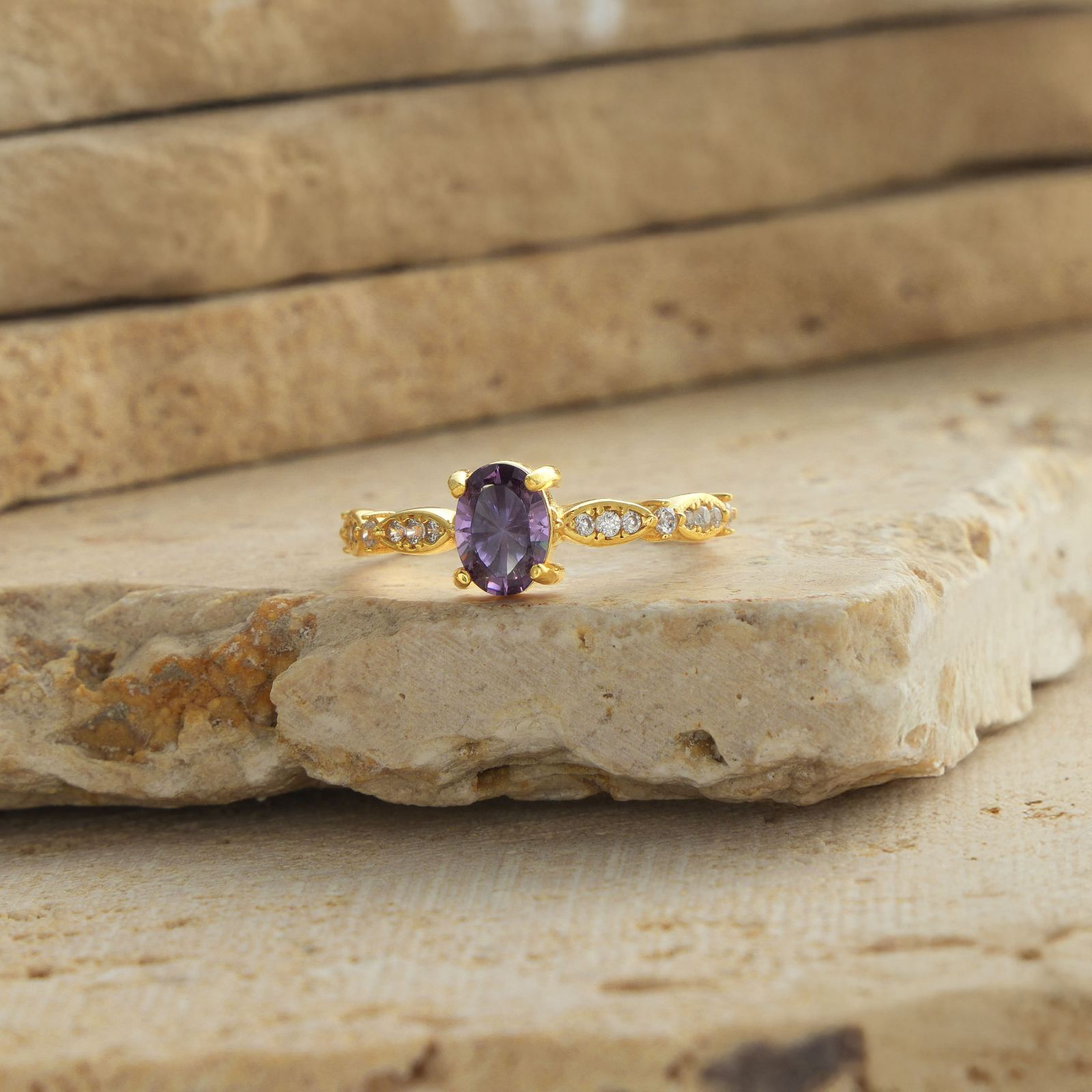 Custom Birthstone Rings featuring a gold vermeil ring with amethyst stone and accent diamonds on a natural stone surface.