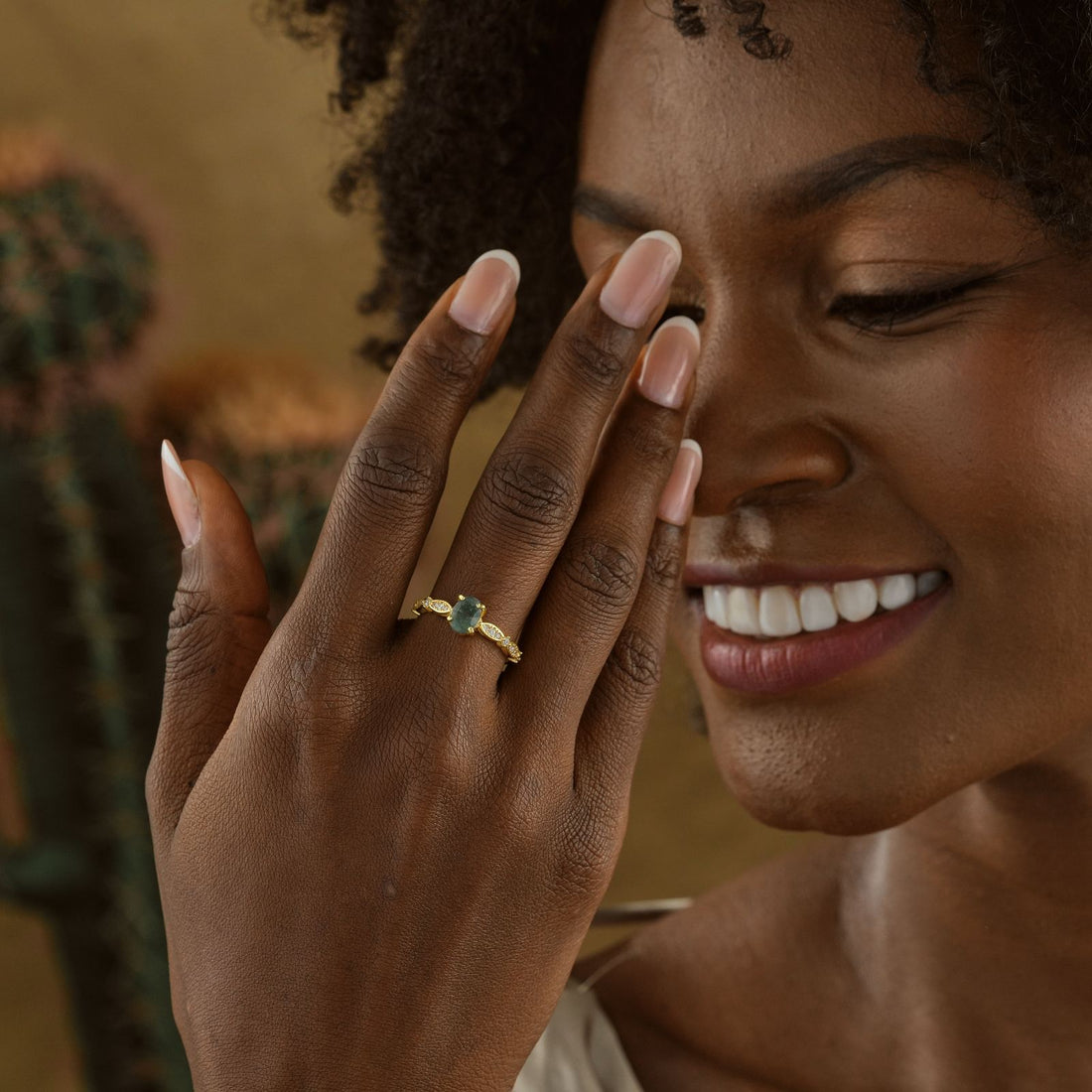 Woman wearing a Custom Birthstone Ring with a green gemstone, smiling while showcasing her elegant hand.