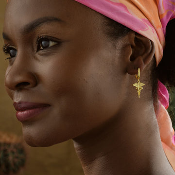 Close-up of a woman wearing stylish Caduceus Earrings, showcasing their intricate design and gold finish.