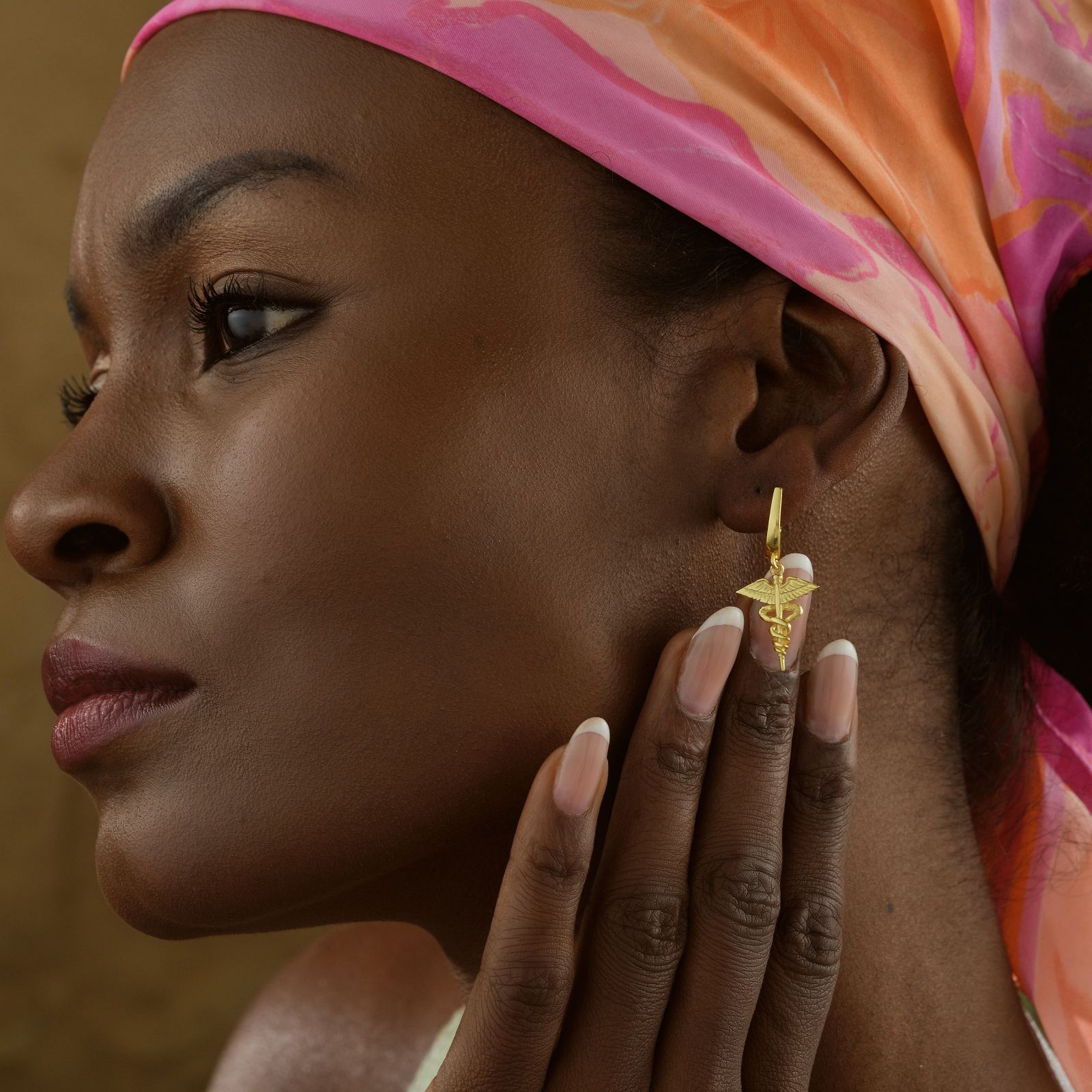 Caduceus Earring worn by a woman with pink scarf, showcasing stylish hoop design and intricate detailing.