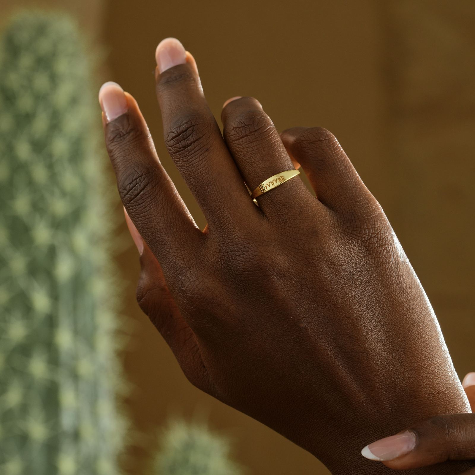 Hand wearing a Personalized Name Ring in gold, showcasing elegant stacking jewelry against a neutral background.