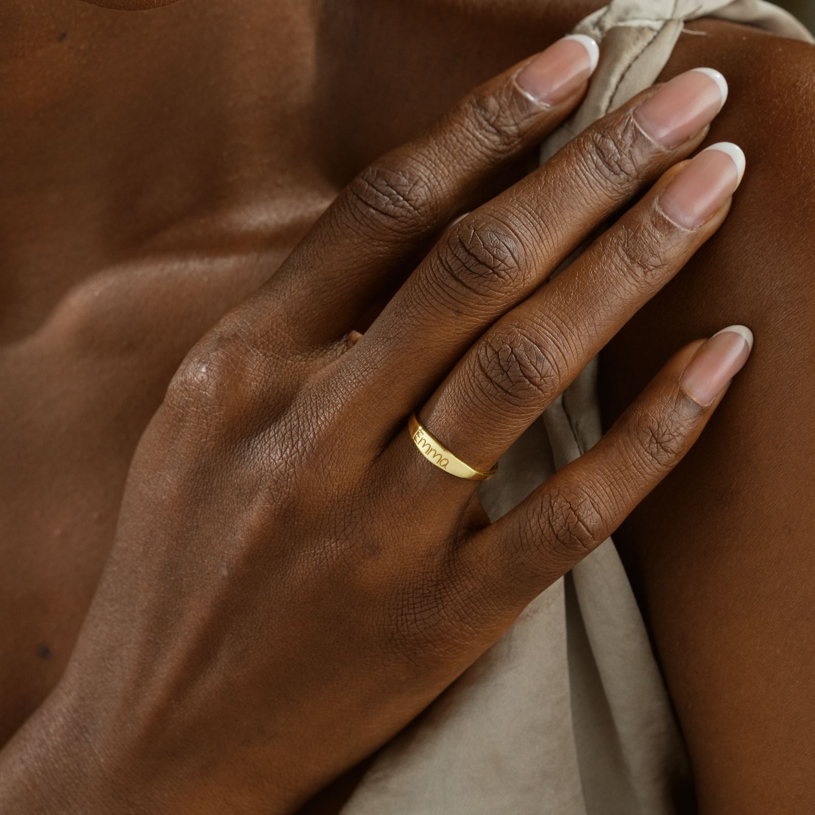 Close-up of a hand wearing a gold Personalized Name Ring on a soft fabric background.