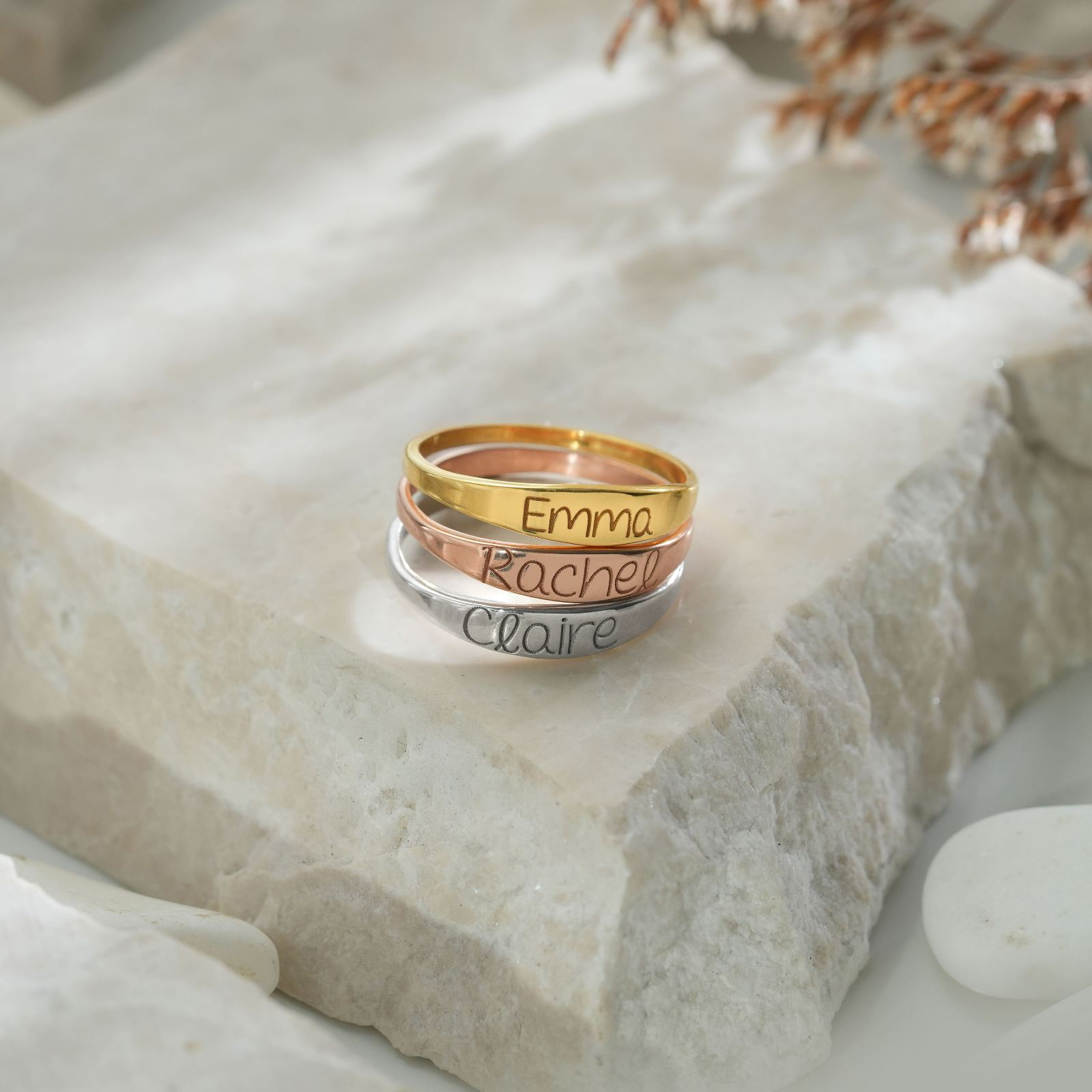 Personalized Name Ring featuring Emma, Rachel, and Claire in gold, rose, and silver stacking rings on a stone surface.