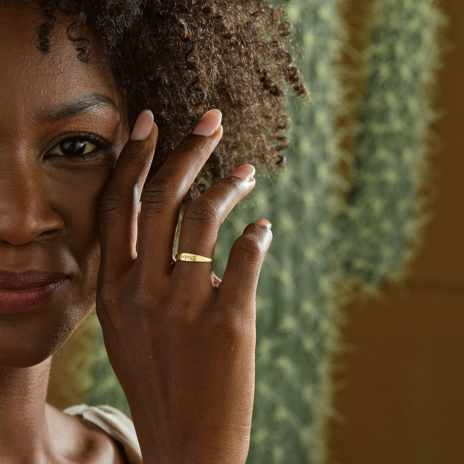 Woman showcasing a Personalized Name Ring in gold while posing against a cactus background.