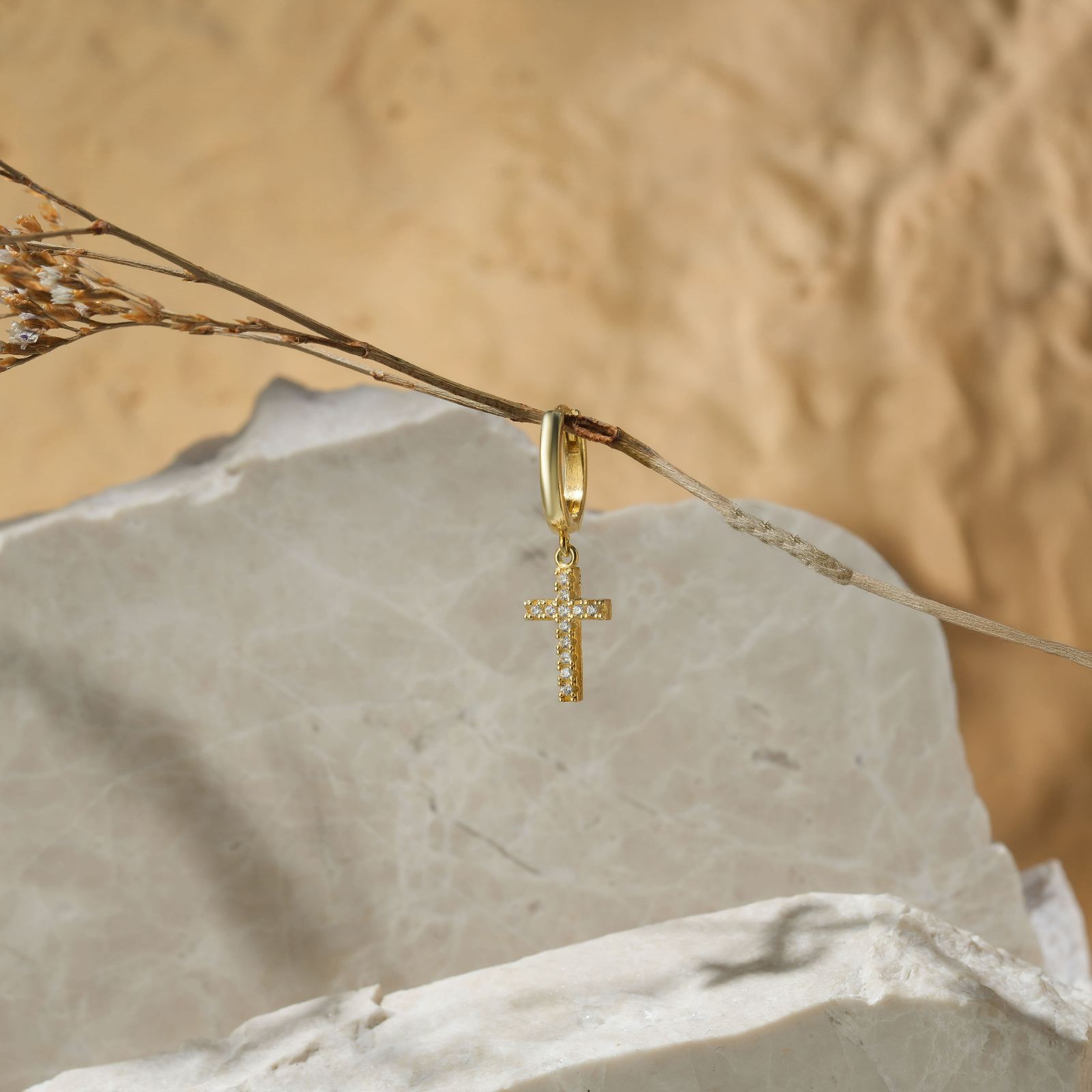 Elegant Diamond Cross Earring hanging from a branch against a textured stone background.