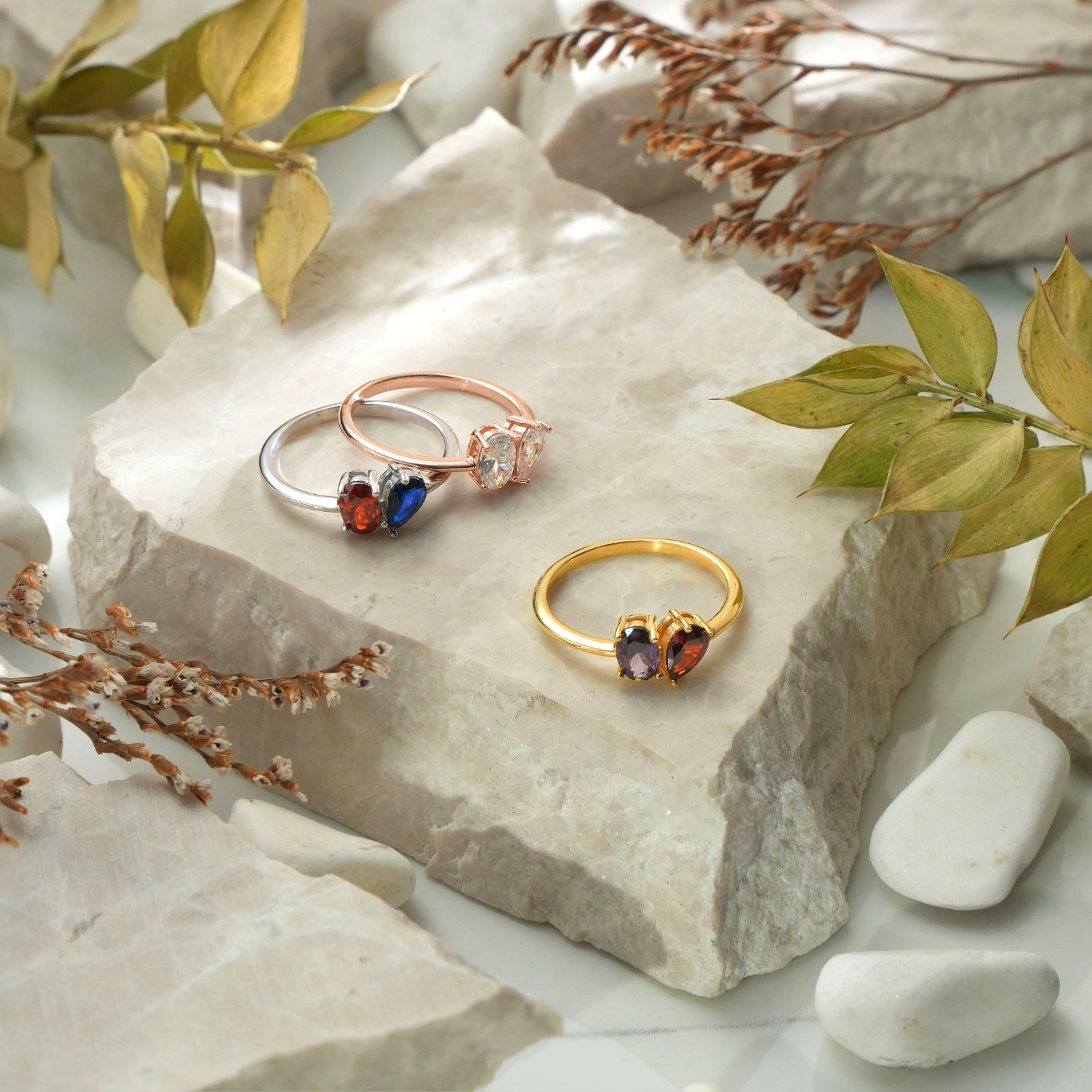 Oval & Pear Cut Birthstone Ring in three colors: silver, gold, and rose gold, displayed on a stone surface.