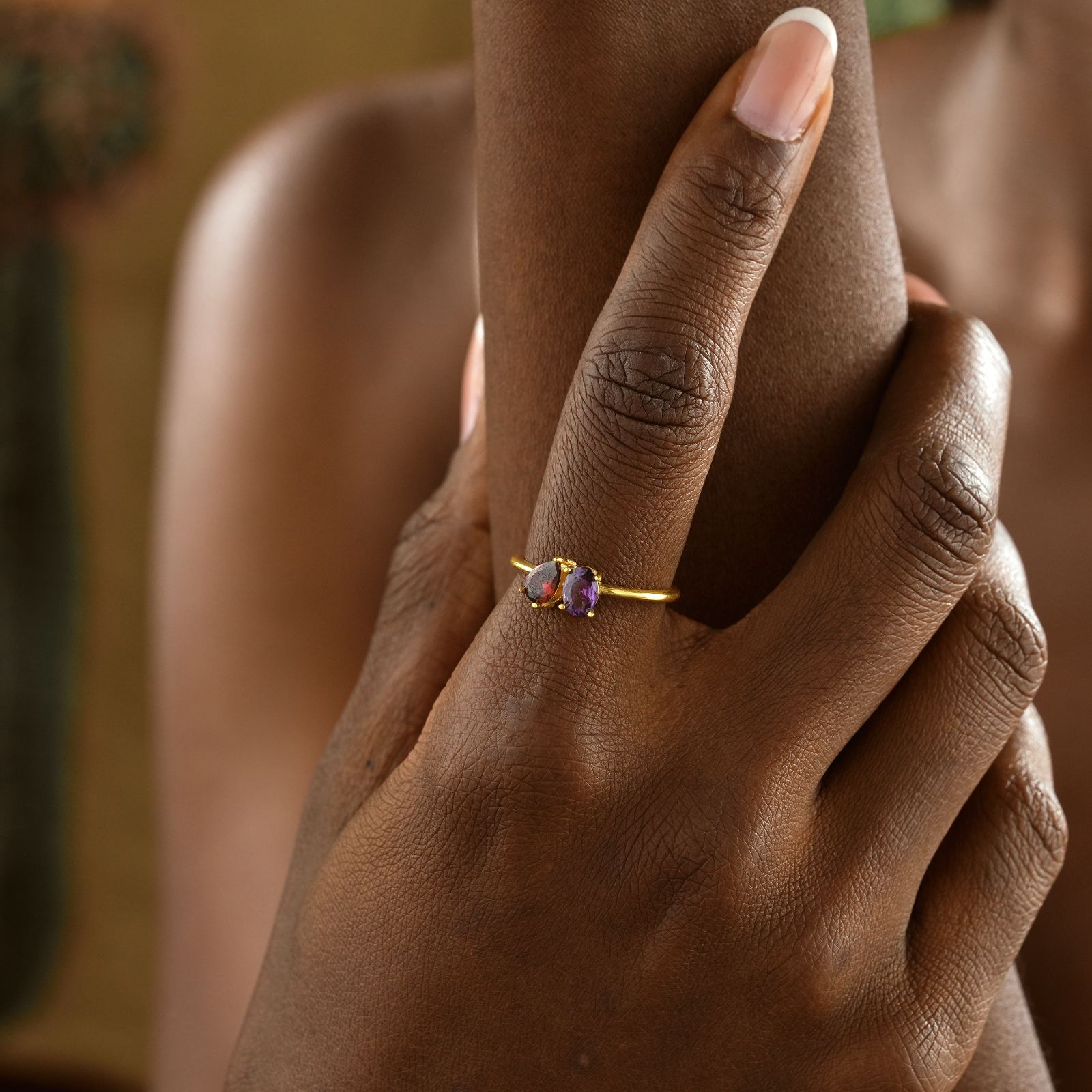 Woman's hand showcasing an Oval & Pear Cut Birthstone Ring with purple stone and gold band.