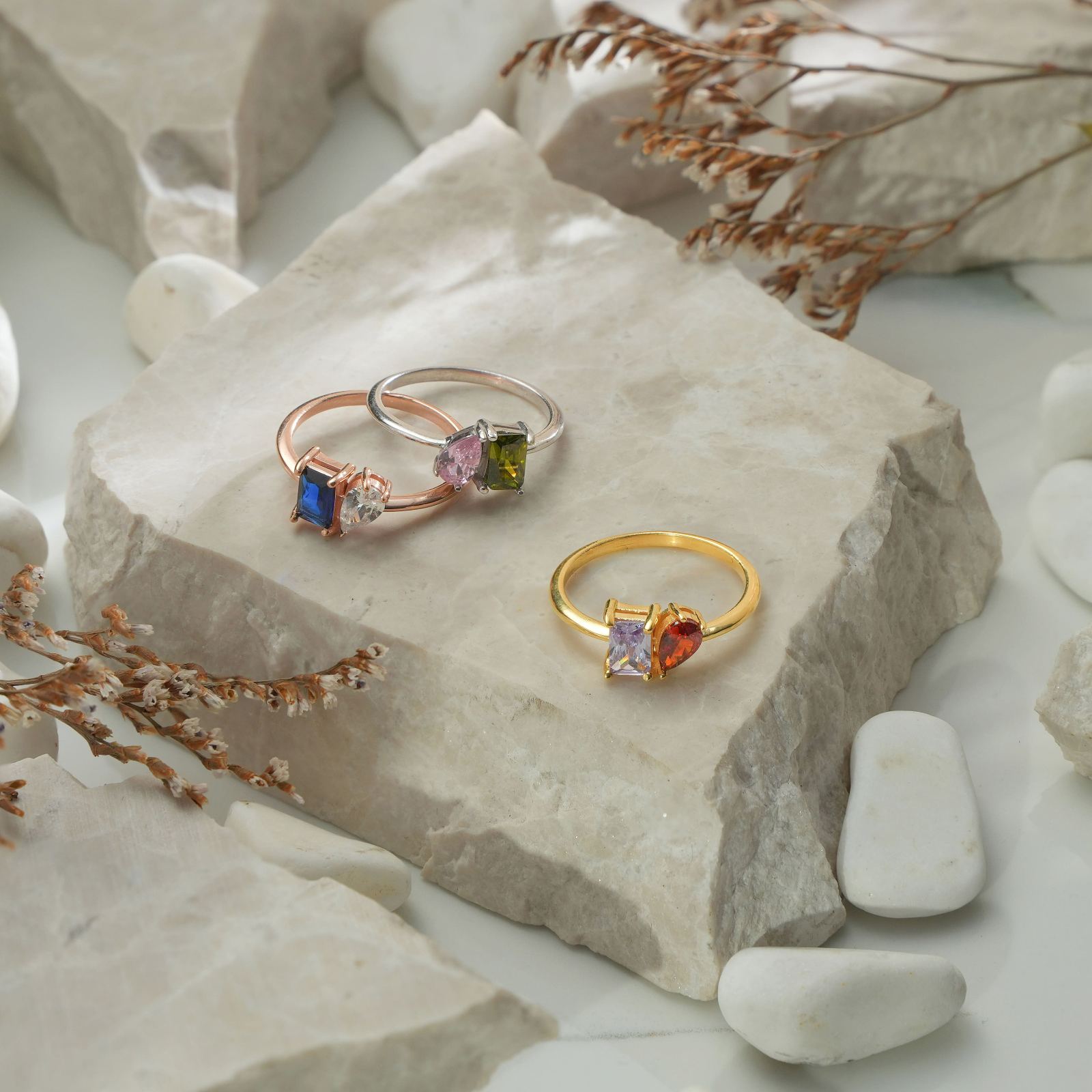 Oval & Emerald Cut Birthstone Ring displayed on stone, featuring colorful gemstones in various metal finishes.