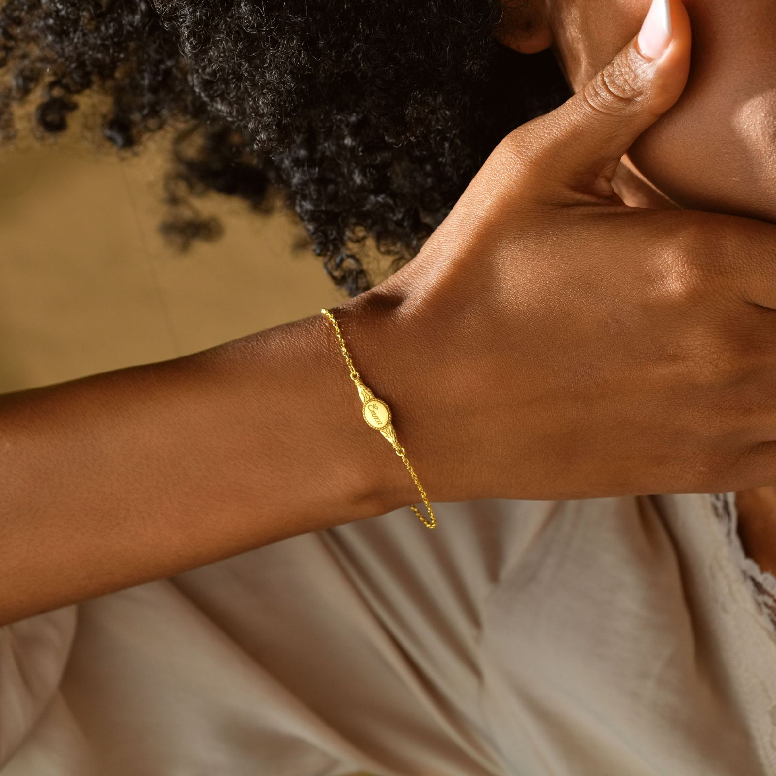 Engraved Oval Name Bracelet in sterling silver worn on a woman's wrist, styled with natural curls.
