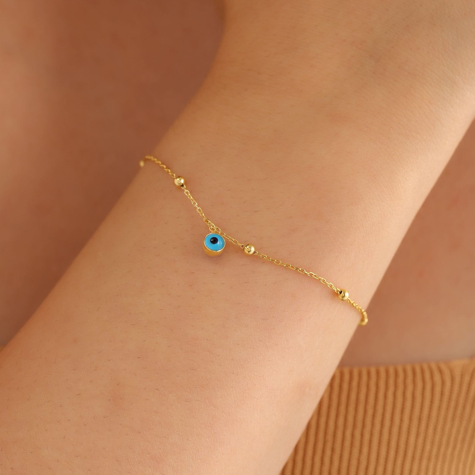 Charming Evil Eye Bracelet in gold vermeil on a wrist with a blue gemstone accent.