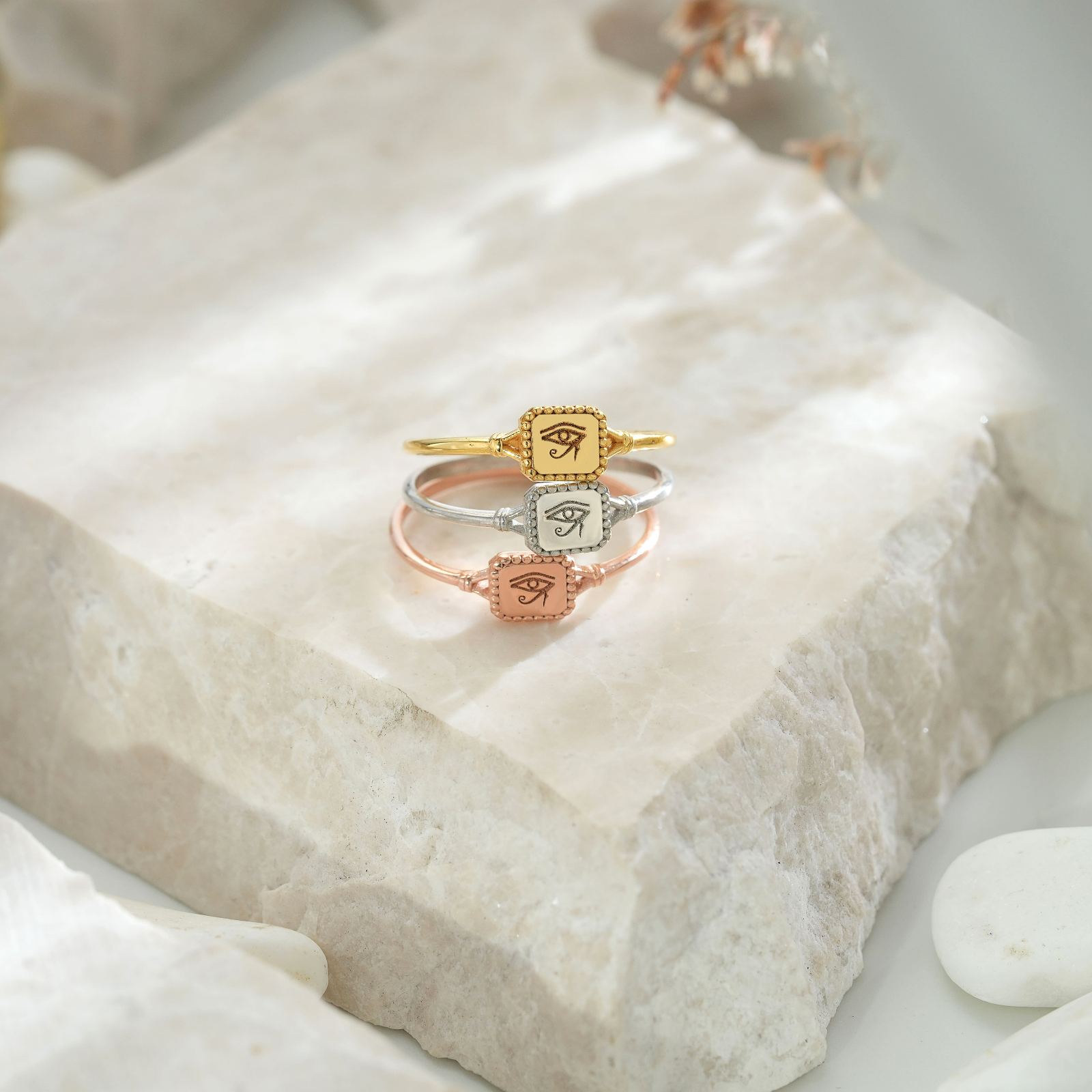 Eye of Ra Signet Ring collection featuring gold, silver, and rose gold on a marble background.