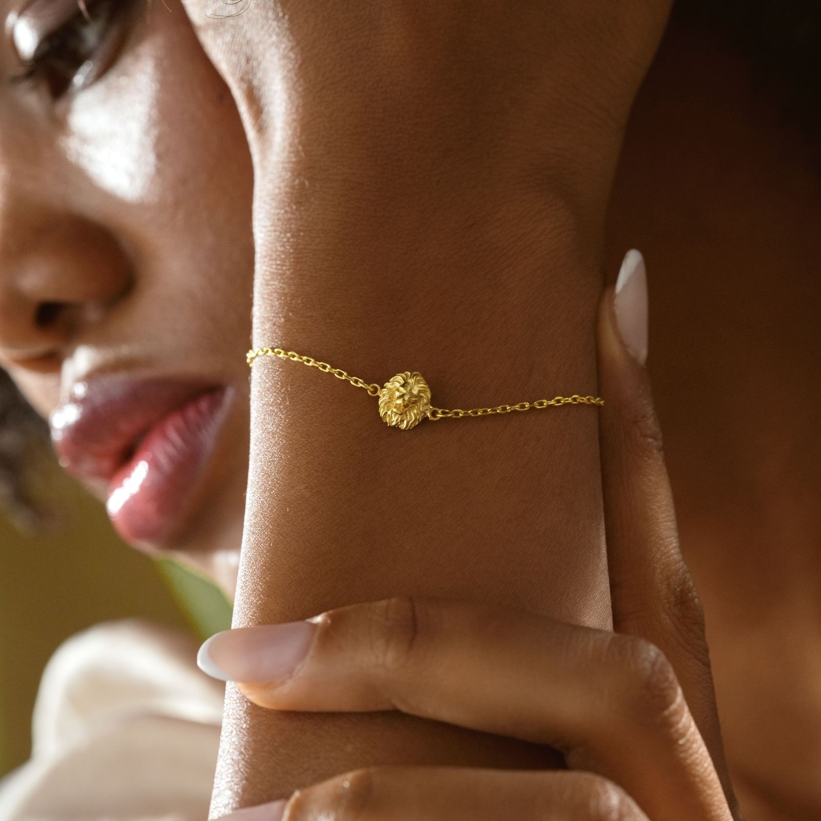 Woman wearing a Lion Pendant Bracelet Minimalist in gold on her wrist, showcasing unique lion design.