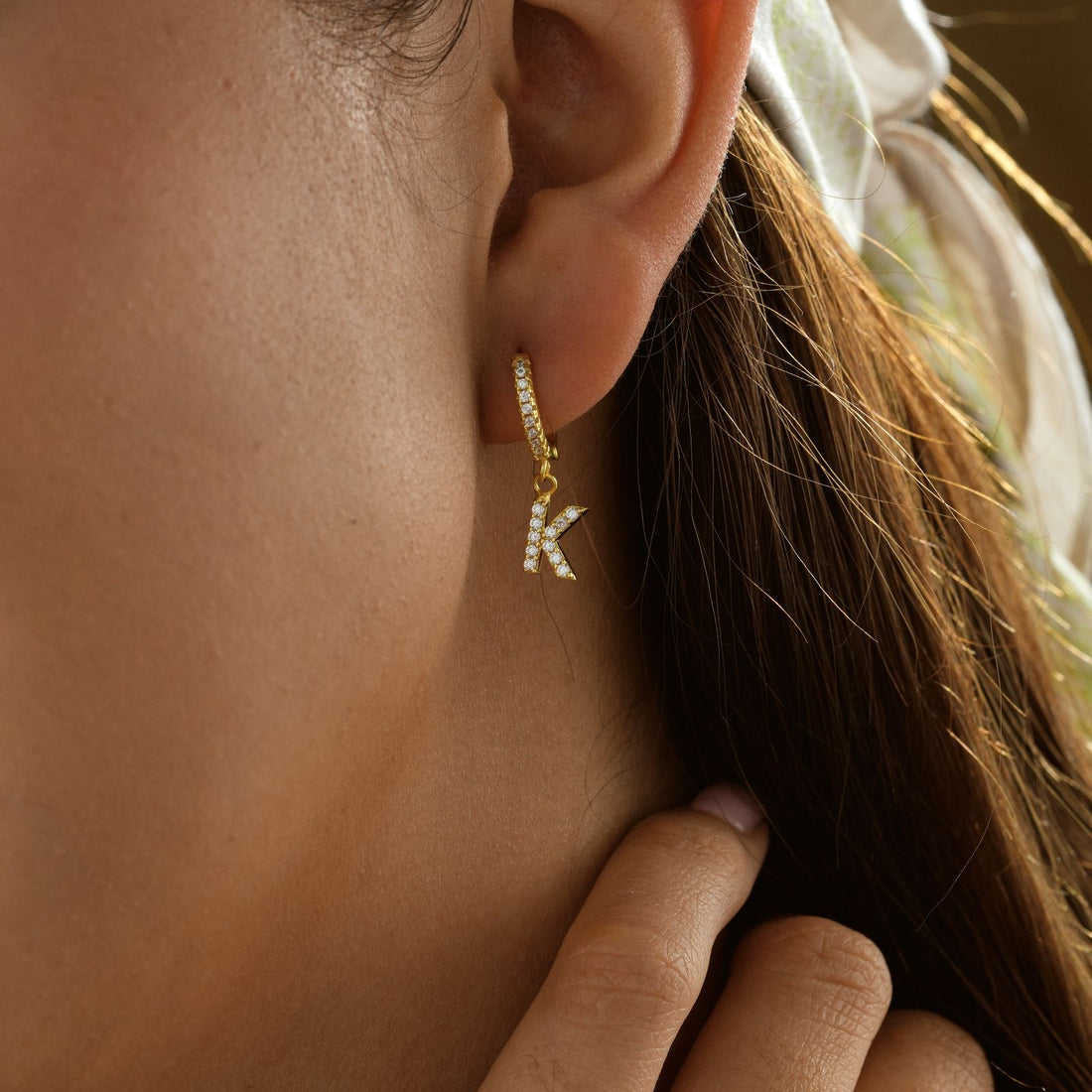 Dainty Initial Huggie Hoop Earring shown on a smiling woman wearing a scarf, highlighting the stylish design.