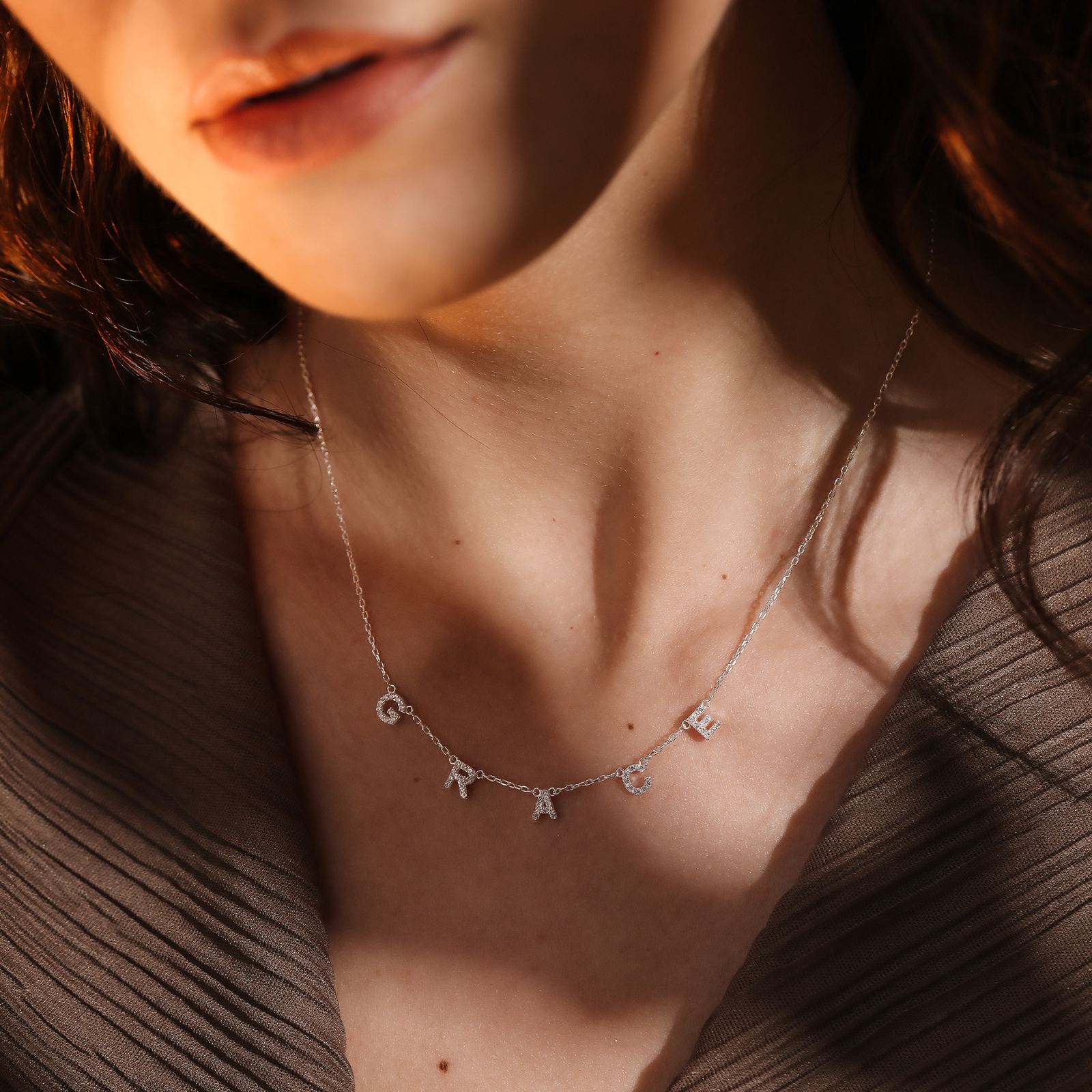 A close-up of a woman wearing a Personalized Tiny Initial Necklace featuring letter charms in sterling silver.