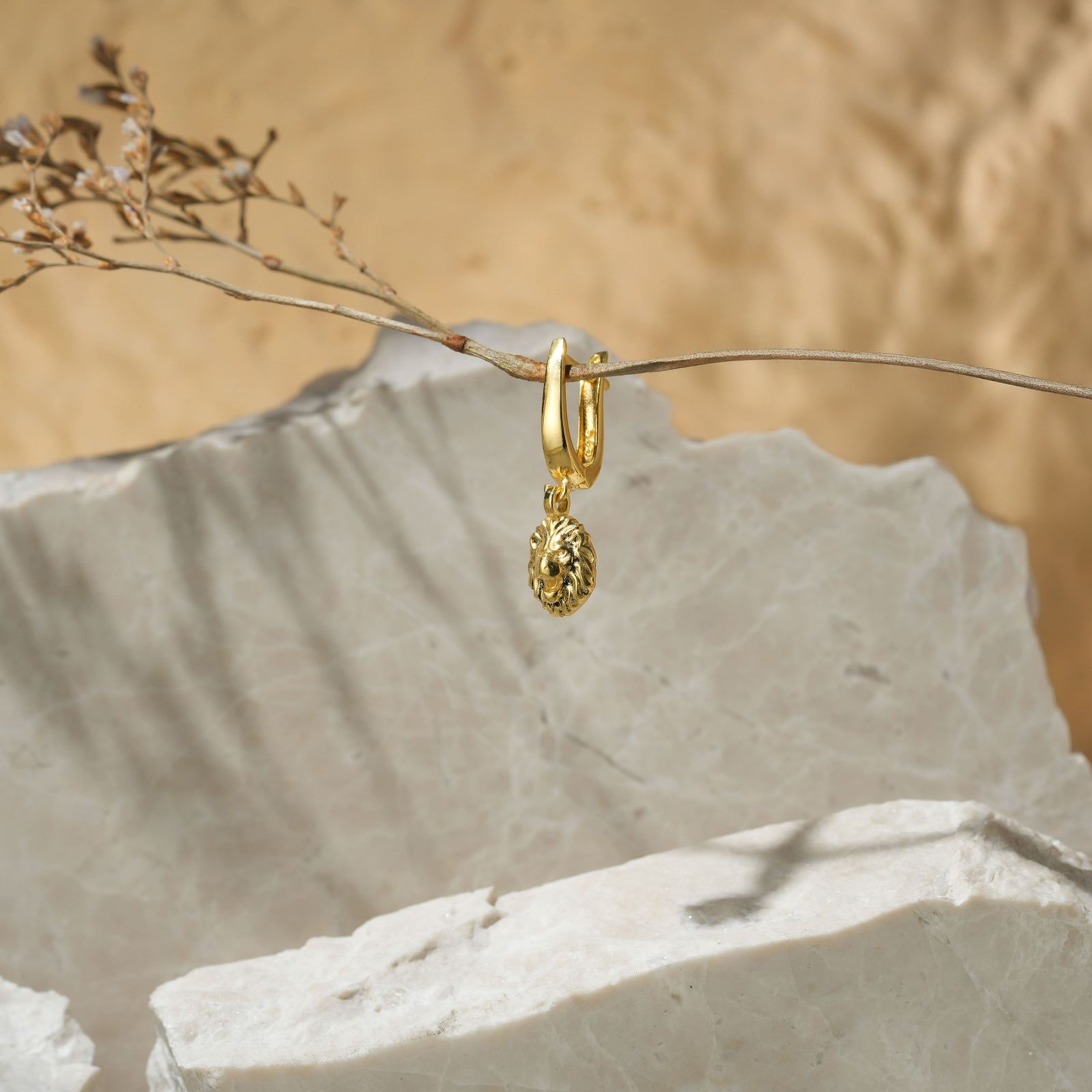 Stylish Lion Dangle Huggie Hoop Earrings hanging on a natural branch with a textured stone backdrop.