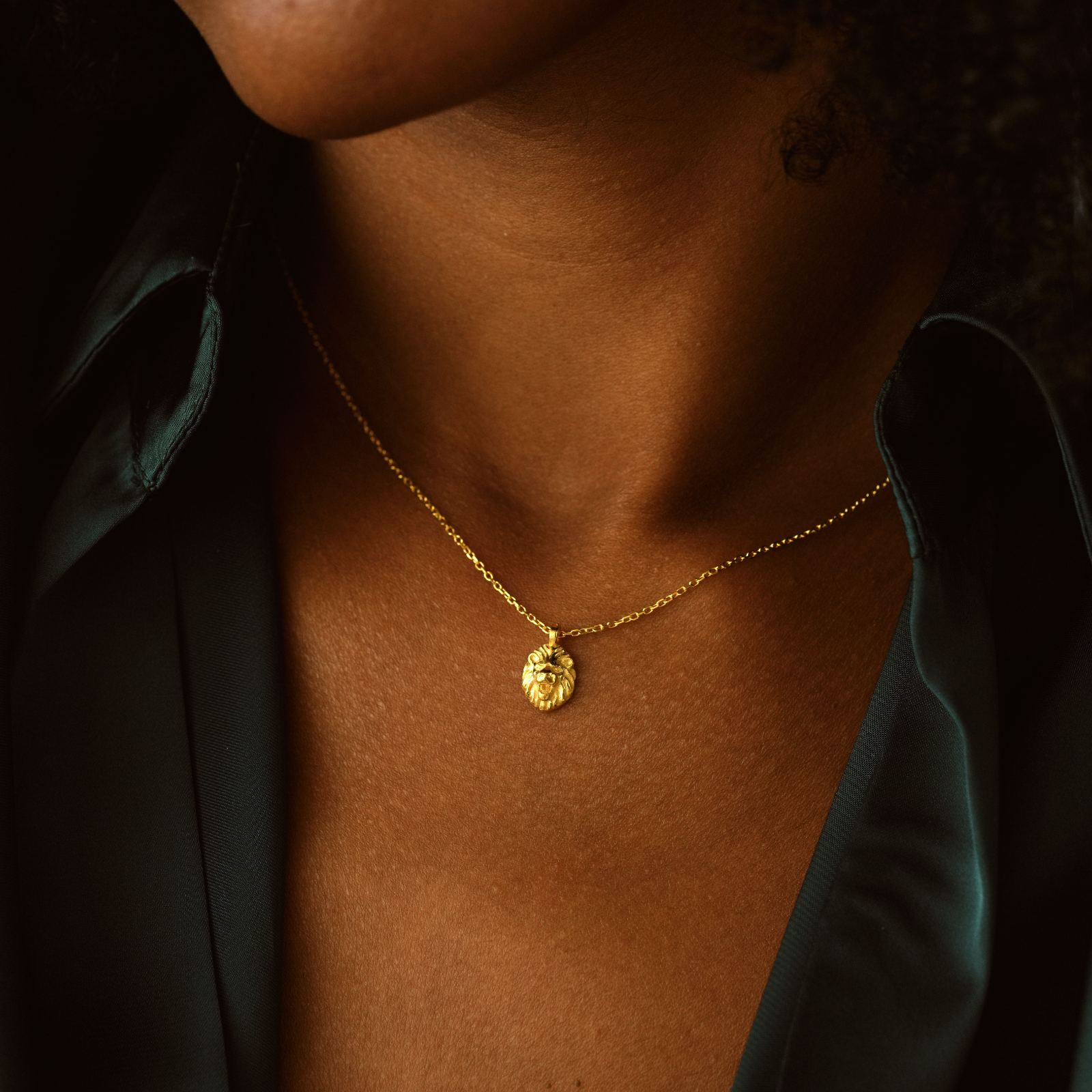 Close-up of a person wearing a Lion Pendant Necklace in gold vermeil against a dark shirt.