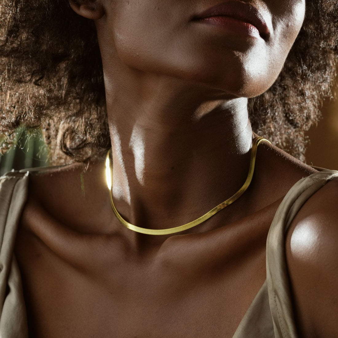 Elegant Minimalist Snake Necklace worn by a woman with curly hair, showcased in a natural setting.