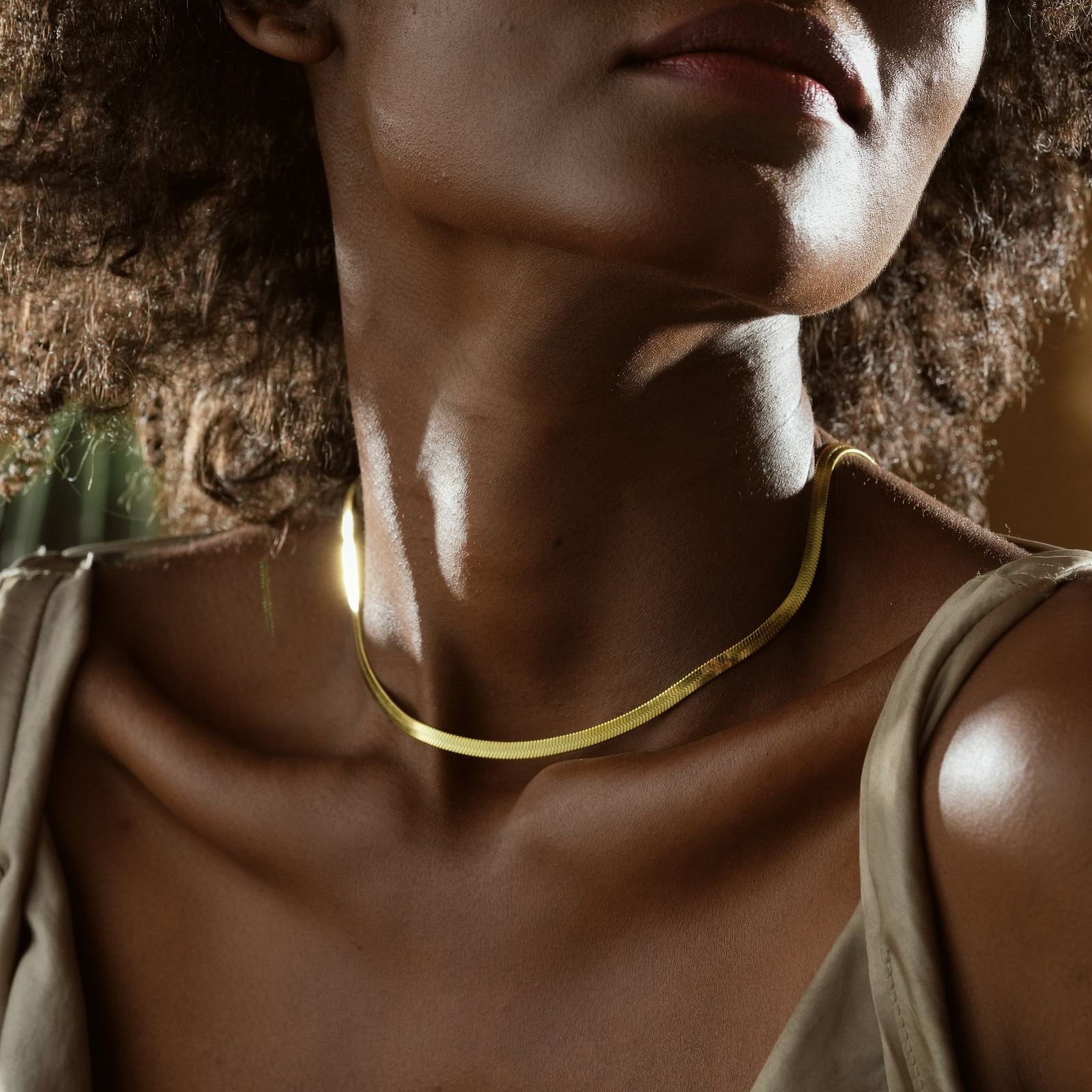 Elegant Minimalist Snake Necklace worn by a woman with curly hair, showcased in a natural setting.