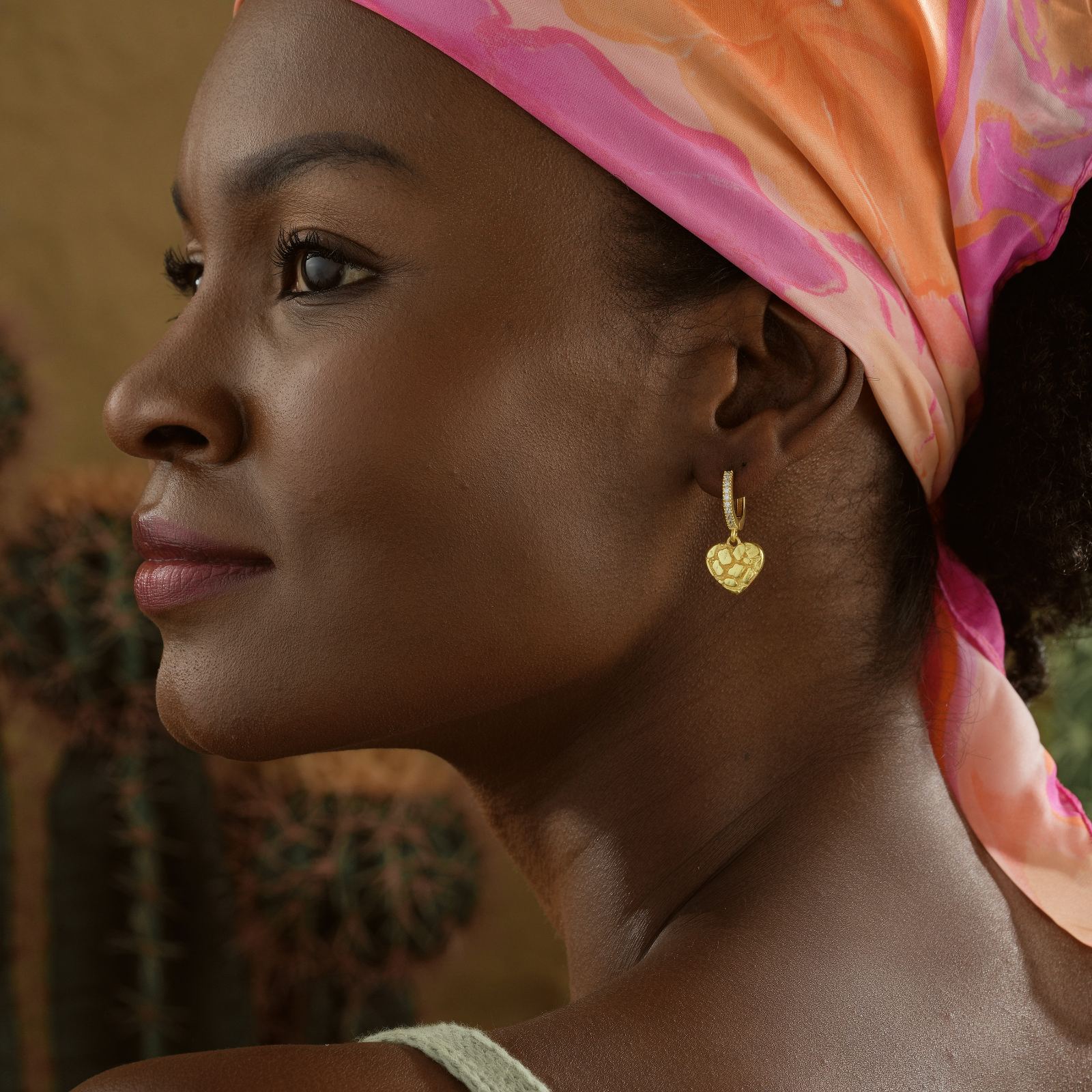 Close-up of a woman wearing Nugget Heart Hoop Earring, showcasing a golden heart design and vibrant headscarf.