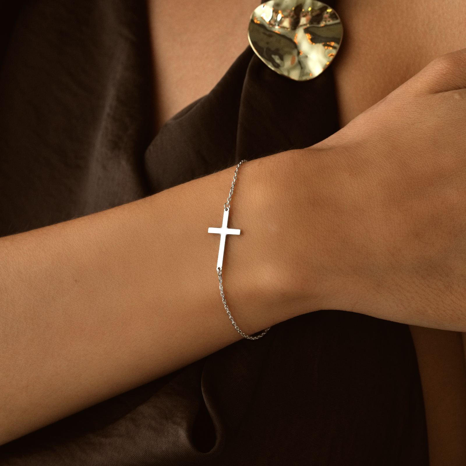 Elegant Sterling Silver Cross Bracelet showcased on a model's wrist against a dark fabric backdrop.