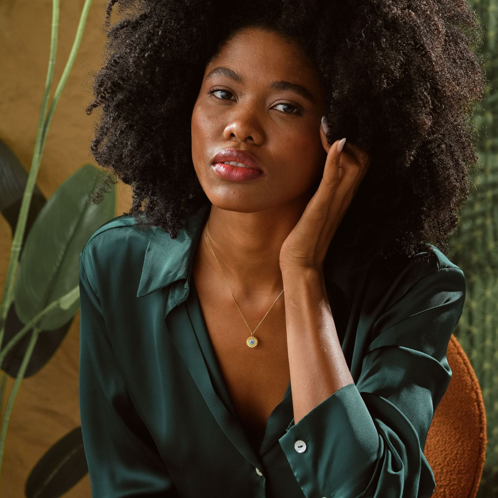 Woman wearing a Charming Sunflower Birthstone Necklace with a stylish green blouse, showcasing a vibrant natural background.