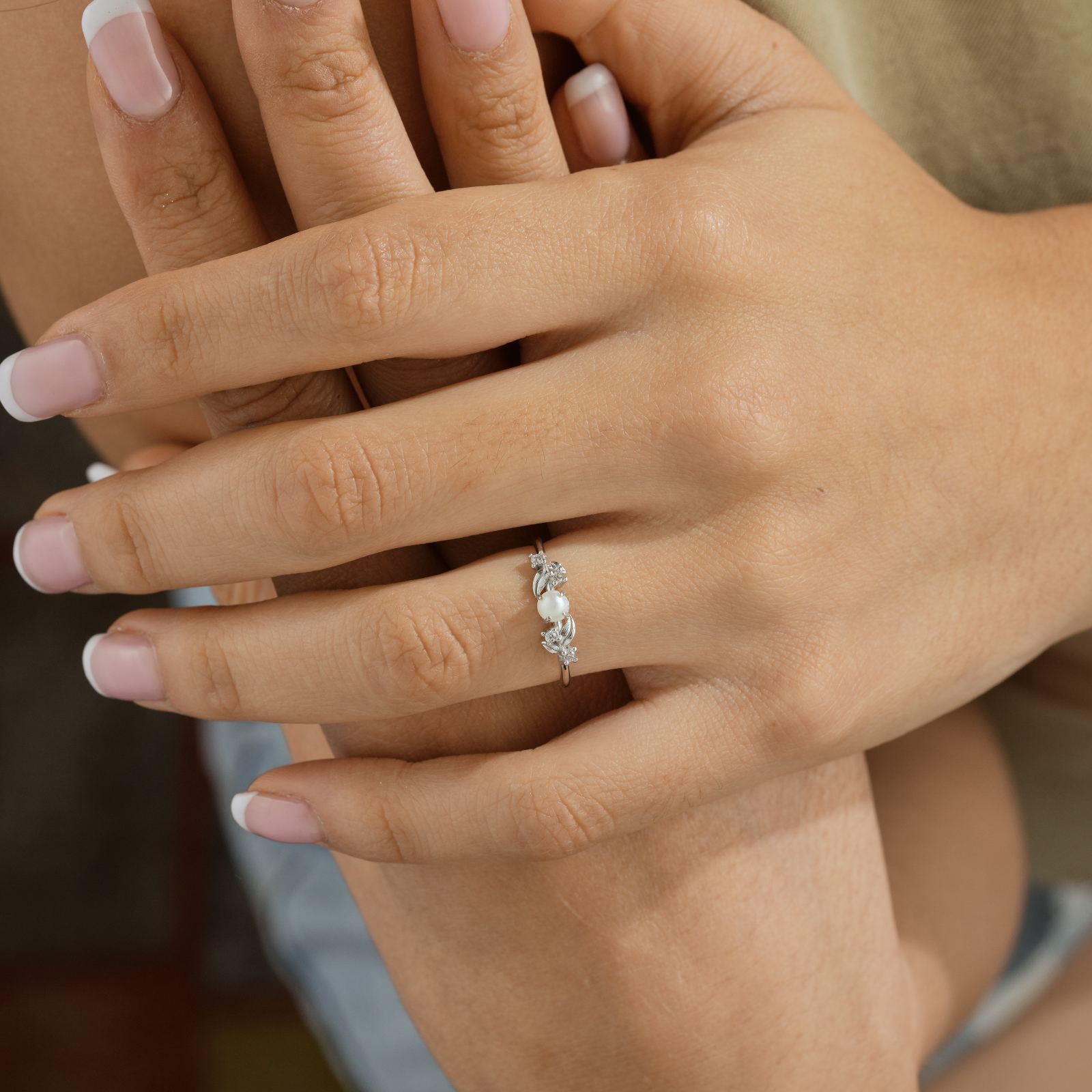Woman's hand wearing a Vintage Pearl Engagement Ring with sparkling gemstones, showcasing elegance and style.