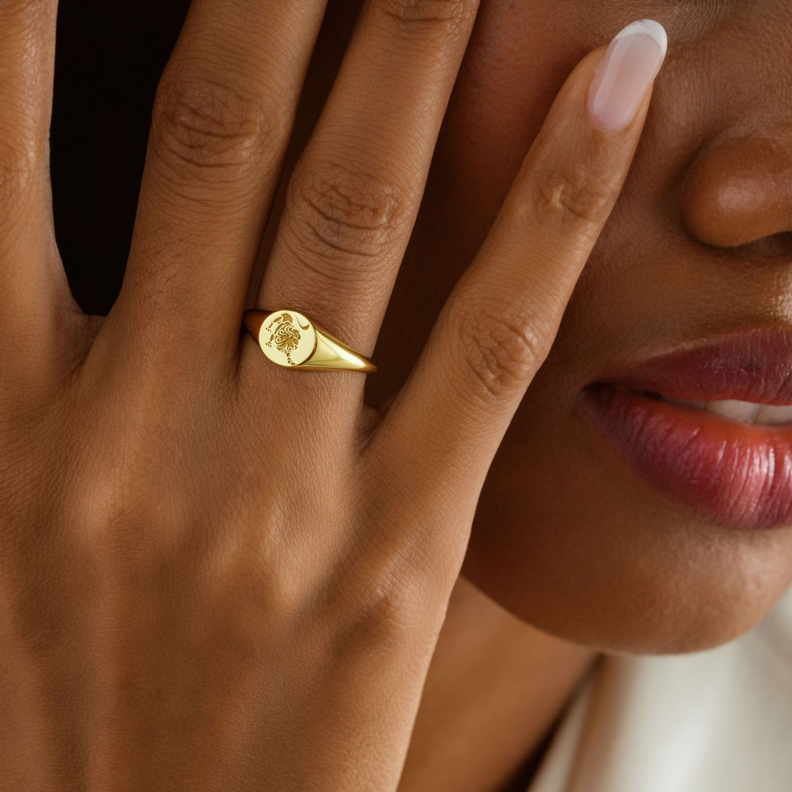 Close-up of woman's hand wearing a gold Zodiac Signet Ring, showcasing its intricate design and elegant finish.